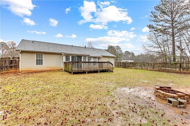 back of property with a fenced backyard, a wooden deck, a yard, and an outdoor fire pit