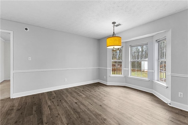 unfurnished dining area with baseboards, visible vents, a textured ceiling, and dark wood-type flooring
