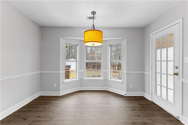 unfurnished dining area featuring baseboards, visible vents, a textured ceiling, and dark wood-type flooring