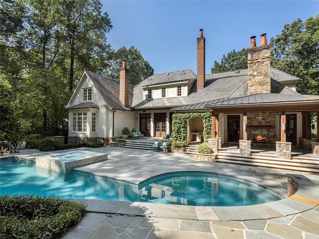 back of property featuring a patio area, a swimming pool with hot tub, and an outdoor stone fireplace