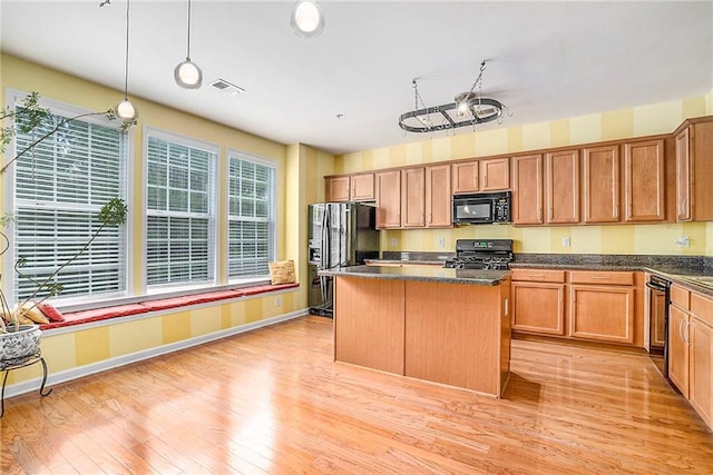 kitchen with dark stone countertops, black appliances, a center island, light hardwood / wood-style flooring, and decorative light fixtures