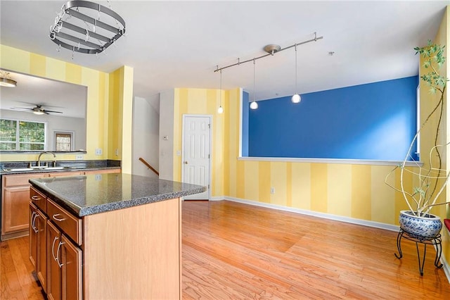 kitchen featuring dark stone counters, light wood-type flooring, sink, a kitchen island, and ceiling fan