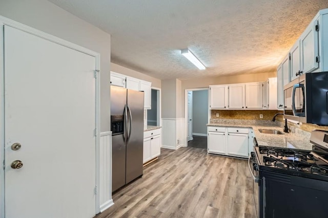 kitchen featuring sink, stainless steel appliances, a textured ceiling, white cabinets, and light wood-type flooring