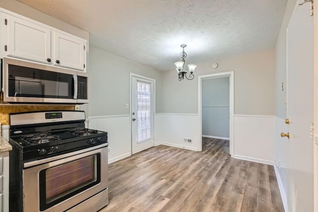 kitchen featuring light wood-type flooring, a textured ceiling, appliances with stainless steel finishes, decorative light fixtures, and white cabinetry