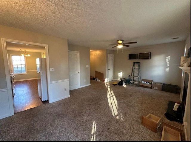 unfurnished living room featuring dark carpet, ceiling fan with notable chandelier, and a textured ceiling