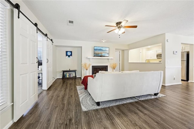 living room featuring ceiling fan, dark wood-type flooring, and a barn door