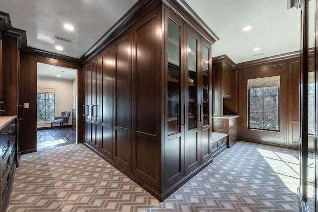 kitchen with dark brown cabinets, glass insert cabinets, crown molding, light countertops, and light carpet