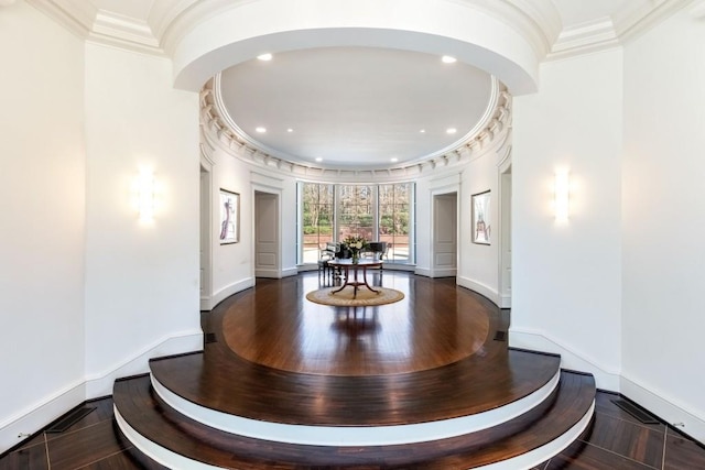 corridor with crown molding, wood finished floors, arched walkways, and baseboards