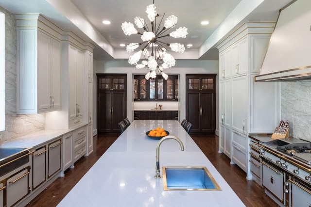 kitchen with a chandelier, a raised ceiling, custom range hood, and a sink