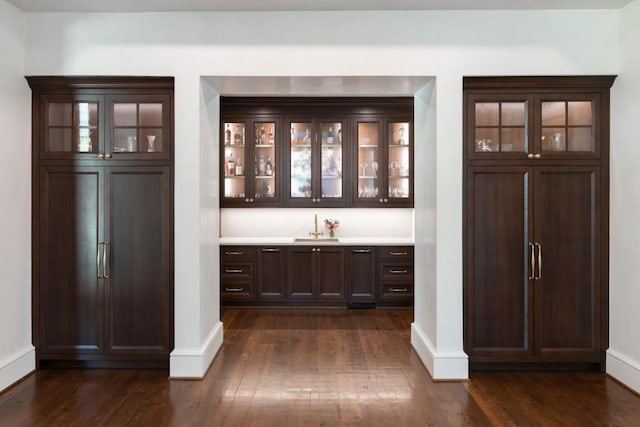 bar with dark wood-type flooring, baseboards, and a sink