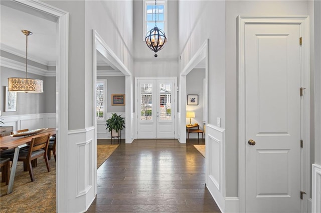 entryway with dark wood-style flooring, wainscoting, crown molding, a decorative wall, and a notable chandelier