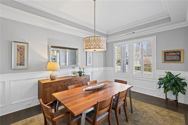 dining room with visible vents, dark wood finished floors, a tray ceiling, ornamental molding, and wainscoting