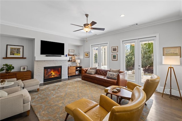 living area with visible vents, ornamental molding, a stone fireplace, french doors, and wood-type flooring