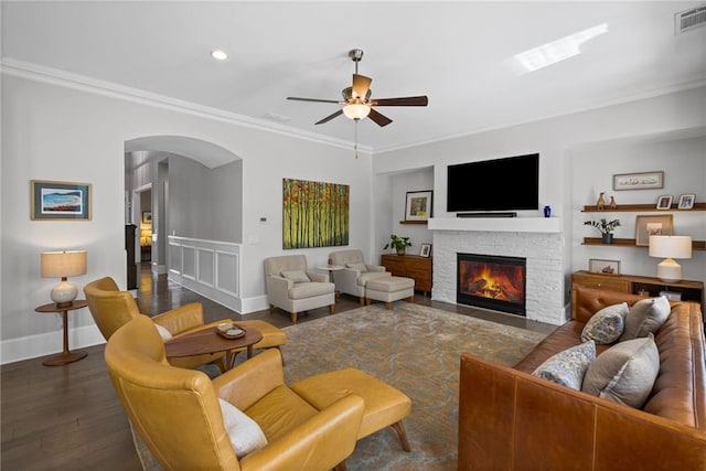 living room featuring visible vents, ornamental molding, wood finished floors, arched walkways, and a fireplace