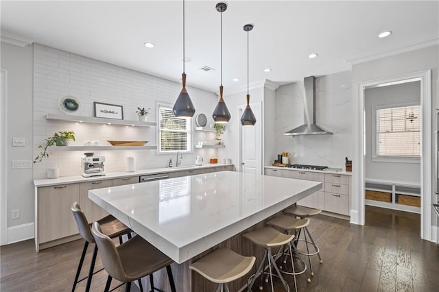 kitchen featuring open shelves, a sink, gas stovetop, a breakfast bar area, and wall chimney range hood