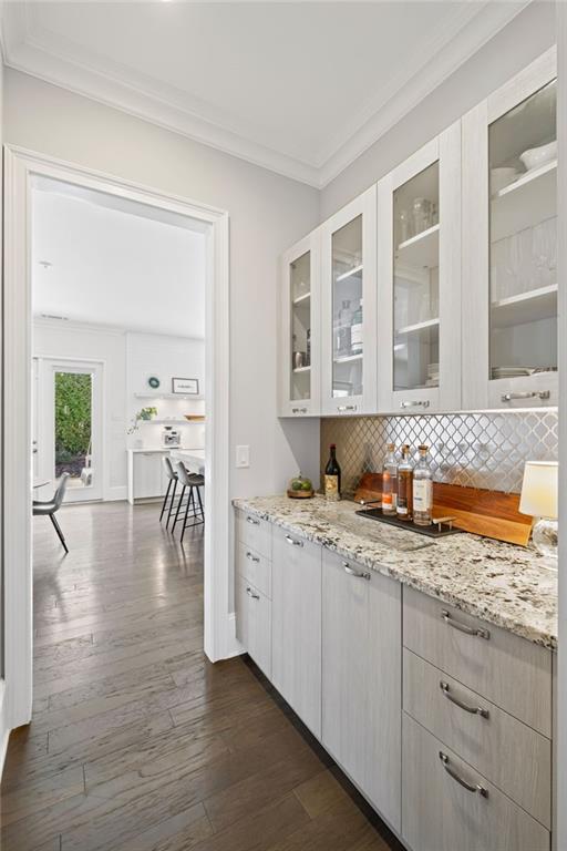 bar featuring decorative backsplash, dark wood-type flooring, baseboards, and ornamental molding