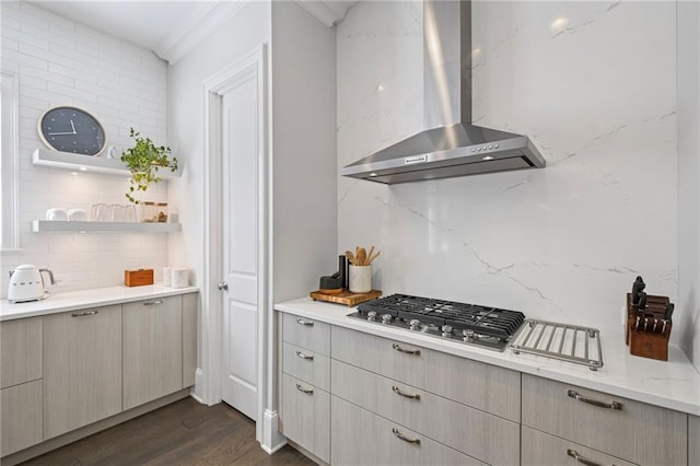 kitchen with wall chimney range hood, light stone countertops, dark wood finished floors, stainless steel gas cooktop, and decorative backsplash