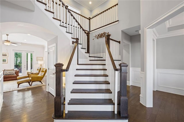 staircase with hardwood / wood-style floors, a wainscoted wall, arched walkways, and ornamental molding