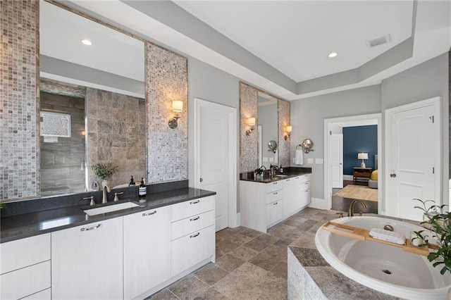 bathroom with a garden tub, stone finish flooring, two vanities, and a sink