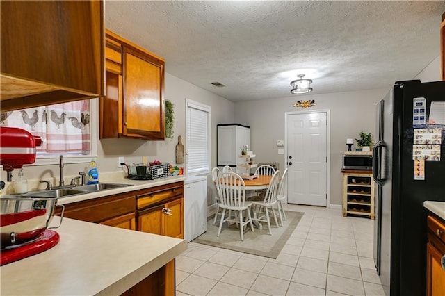 kitchen with black refrigerator, light tile patterned floors, a textured ceiling, and sink