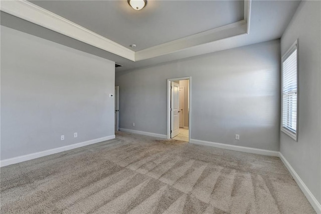 carpeted spare room featuring crown molding, a tray ceiling, and baseboards