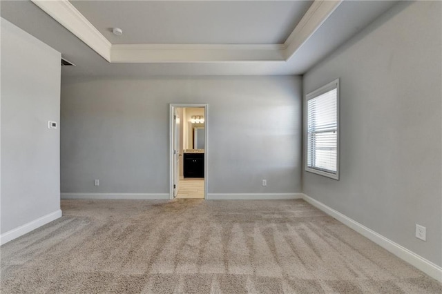 carpeted empty room featuring a tray ceiling, crown molding, and baseboards