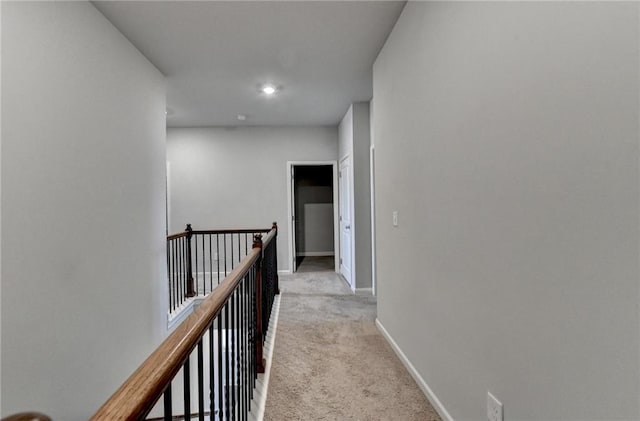 hall with an upstairs landing, light colored carpet, and baseboards