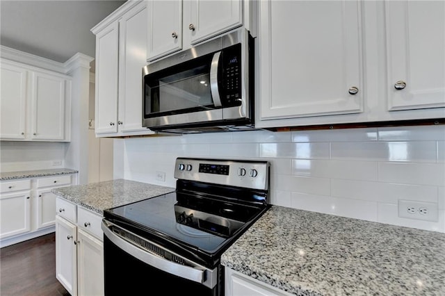 kitchen featuring stainless steel microwave, white cabinets, backsplash, and range with electric stovetop