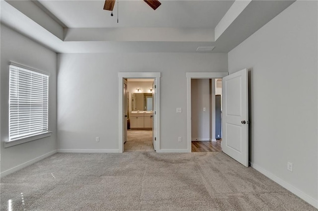 unfurnished bedroom featuring a tray ceiling, ensuite bathroom, ceiling fan, and light colored carpet