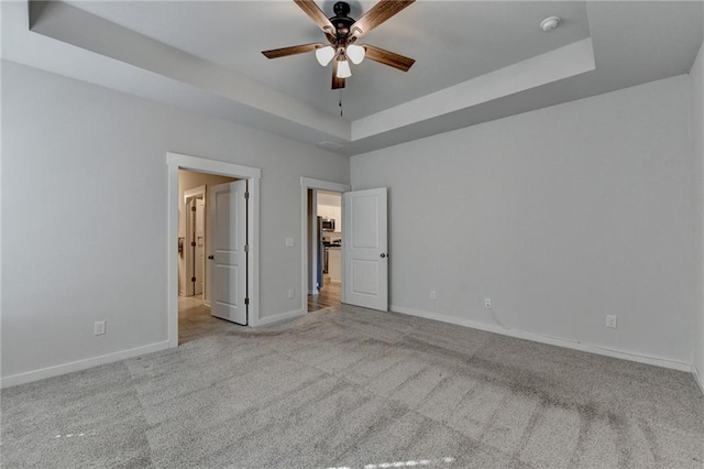 unfurnished bedroom featuring light colored carpet, a raised ceiling, and ceiling fan