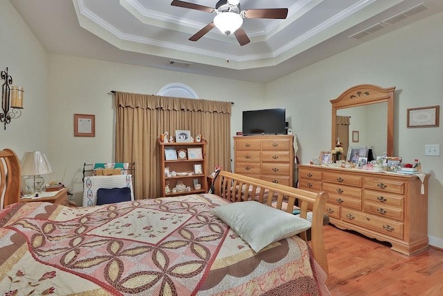 bedroom with crown molding, a tray ceiling, light hardwood / wood-style floors, and ceiling fan