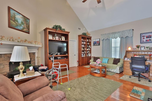 living room featuring ceiling fan, high vaulted ceiling, light wood-type flooring, and a stone fireplace