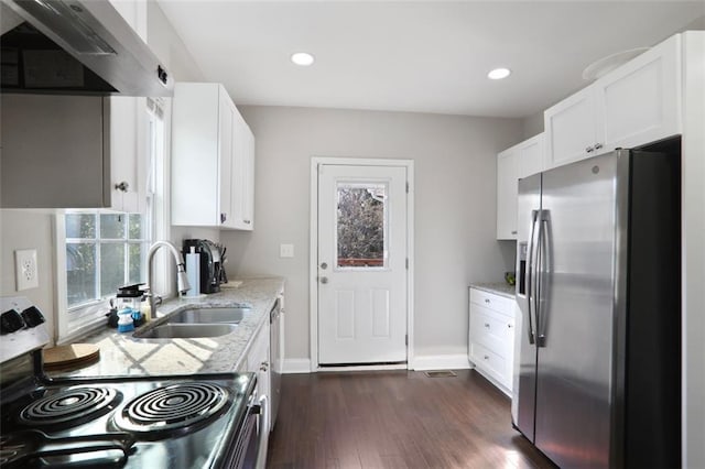 kitchen featuring appliances with stainless steel finishes, white cabinetry, a sink, wall chimney range hood, and light stone countertops