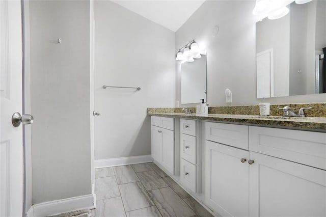 bathroom featuring marble finish floor, double vanity, vaulted ceiling, a sink, and baseboards