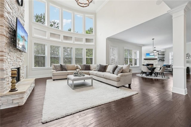 living room with ornamental molding, a stone fireplace, dark hardwood / wood-style flooring, and ornate columns