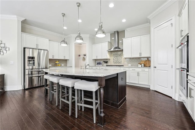 kitchen featuring appliances with stainless steel finishes, a kitchen island with sink, white cabinets, and wall chimney exhaust hood