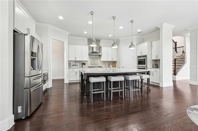 kitchen with pendant lighting, stainless steel appliances, an island with sink, and white cabinets