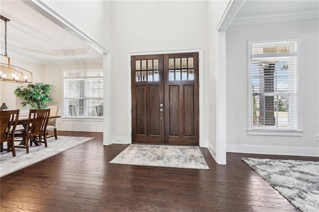 foyer entrance with ornamental molding, dark hardwood / wood-style floors, and a chandelier