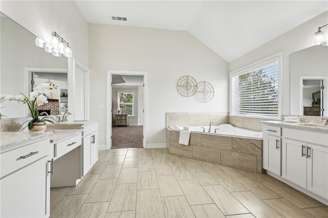 bathroom featuring vanity, lofted ceiling, and tiled bath