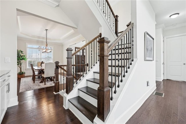 stairs with crown molding, a tray ceiling, an inviting chandelier, and hardwood / wood-style flooring