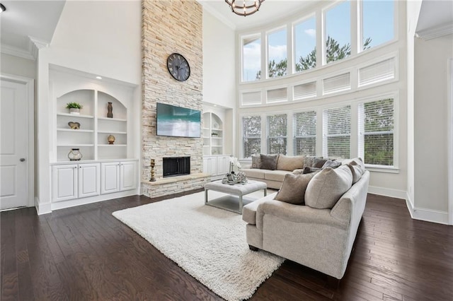 living room with crown molding, a stone fireplace, dark wood-type flooring, and built in features