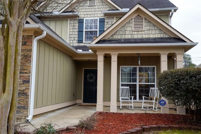 doorway to property with stone siding, covered porch, and a shingled roof