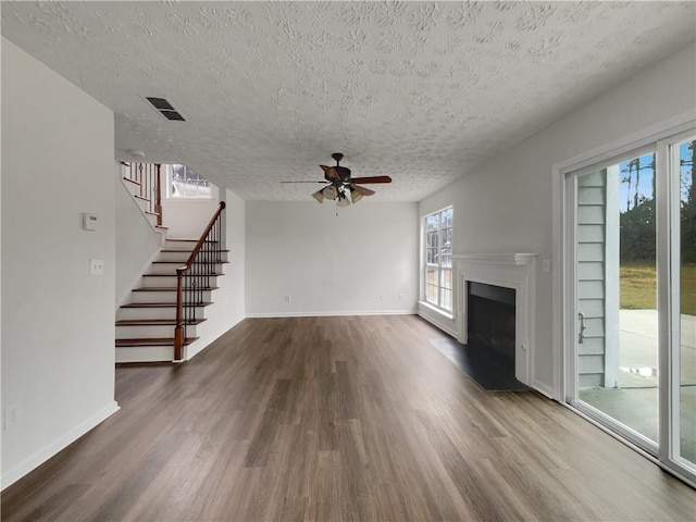 unfurnished living room with a fireplace with raised hearth, a textured ceiling, wood finished floors, baseboards, and stairway