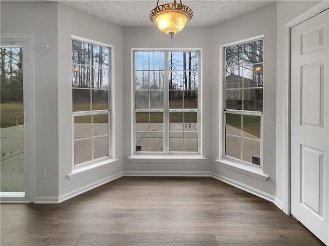 unfurnished dining area featuring a textured ceiling, baseboards, and wood finished floors