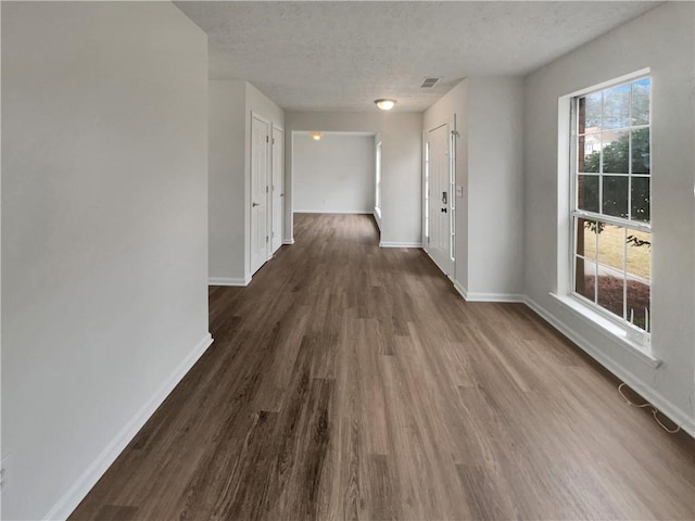 hallway featuring visible vents, a textured ceiling, baseboards, and dark wood-type flooring