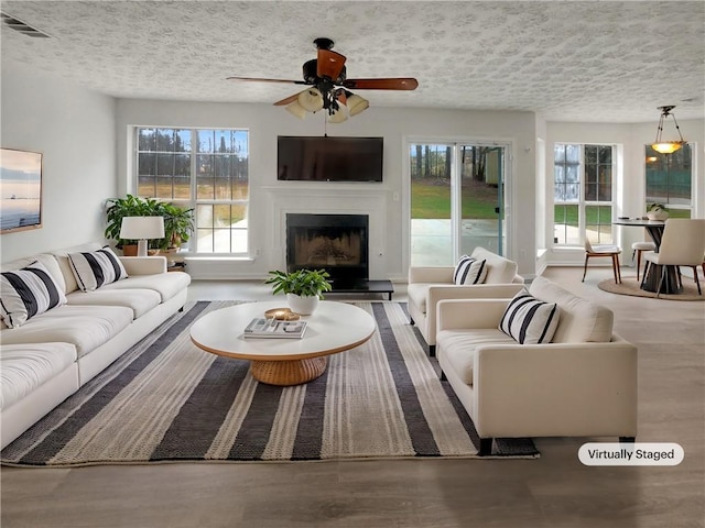 living area featuring plenty of natural light, visible vents, a fireplace with raised hearth, and wood finished floors