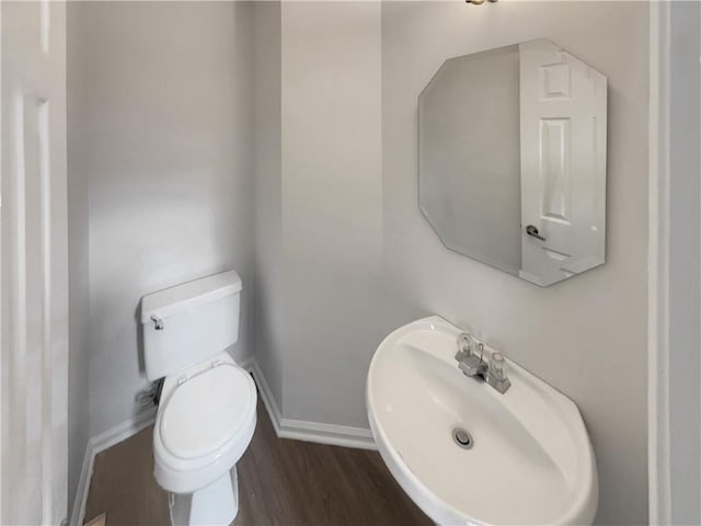 half bath with toilet, baseboards, a sink, and wood finished floors