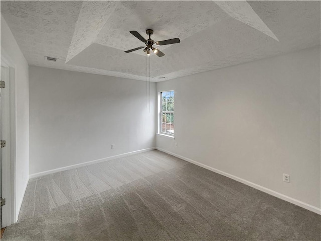 empty room featuring a textured ceiling, carpet floors, a ceiling fan, baseboards, and a raised ceiling