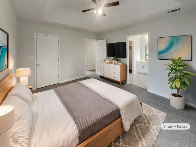 carpeted bedroom with a raised ceiling, ensuite bath, visible vents, and baseboards