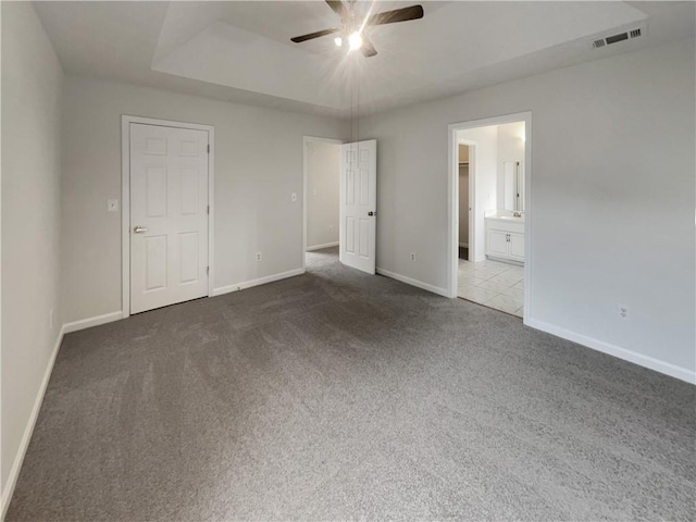 unfurnished bedroom featuring carpet floors, a tray ceiling, visible vents, ensuite bathroom, and baseboards